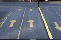 arrow symbols painted on a roadway with a light pole in the distance and a street lined by yellow curbing