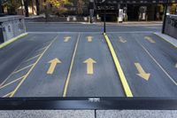 arrow symbols painted on a roadway with a light pole in the distance and a street lined by yellow curbing