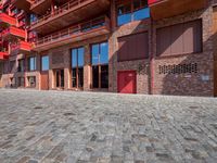 a brick building with a red door in the courtyard and side walk next to the building