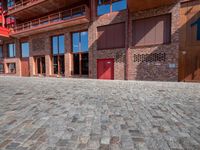 a brick building with a red door in the courtyard and side walk next to the building