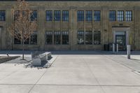 large brick building with a clock sitting in front of it and a tree sitting on the sidewalk