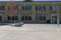 large brick building with a clock sitting in front of it and a tree sitting on the sidewalk