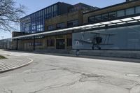 the ground in front of this empty building is cracked and some people are walking and waiting at the bus stop