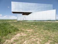 an unusual, mirrored sculpture stands alone in a grassy field under a blue sky with clouds