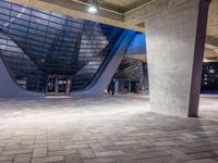 a tiled area with light on and concrete pillars and an empty sidewalk area under a blue lighted sky