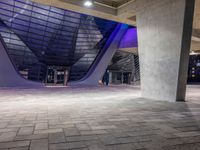 a tiled area with light on and concrete pillars and an empty sidewalk area under a blue lighted sky