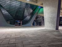 a tiled area with light on and concrete pillars and an empty sidewalk area under a blue lighted sky