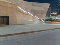 stairs are made out of concrete and beside two buildings at night time with lights on them