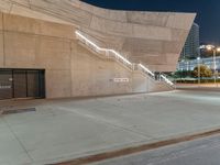 stairs are made out of concrete and beside two buildings at night time with lights on them