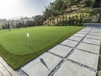 a artificial putting green in a tennis court with grass and flags on the edge of the green