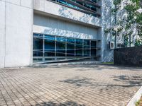 a brick walkway with trees and a building in the background with glass windows and a large white building