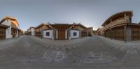 a fisheye panoramic lens photo of an asian area at sunrise with a building and several houses