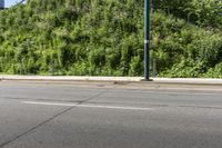 an asian boy riding a skateboard on a street near some bushes and grass that are in the background