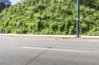 an asian boy riding a skateboard on a street near some bushes and grass that are in the background