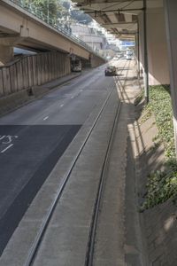 a train on a track next to a sidewalk near buildings and an overpass above