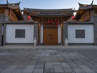 the asian style building has multiple doors and stone flooring, two red lanterns and lights