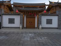 the asian style building has multiple doors and stone flooring, two red lanterns and lights