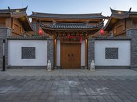 the asian style building has multiple doors and stone flooring, two red lanterns and lights