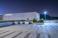 a very large empty concrete courtyard next to some trees and lights at night time as well