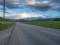 the road is empty during the day and has mountains in the distance as well as a fence