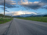 the road is empty during the day and has mountains in the distance as well as a fence