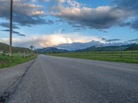 the road is empty during the day and has mountains in the distance as well as a fence