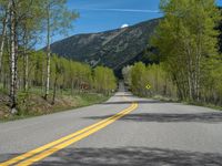 a yellow and black sign is on the street near some mountains and trees in the distance