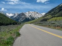 the road is paved with yellow markings and has a snowy mountain range in the background