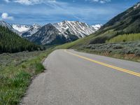 the road is paved with yellow markings and has a snowy mountain range in the background