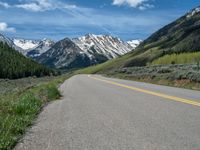 the road is paved with yellow markings and has a snowy mountain range in the background