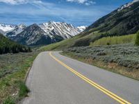 the road is paved with yellow markings and has a snowy mountain range in the background