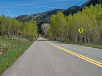 a yellow and black sign is on the street near some mountains and trees in the distance