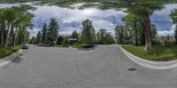 a 360 - view photograph of a street with trees and houses across it with the sky with clouds