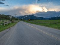 the road is empty during the day and has mountains in the distance as well as a fence