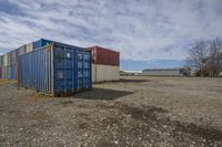 blue shipping container sitting in the middle of an industrial area with grass in the foreground and building in the distance