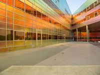 the entrance to a colorful glass building with benches under it, at sunset and in the background