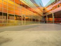 the entrance to a colorful glass building with benches under it, at sunset and in the background