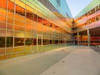 the entrance to a colorful glass building with benches under it, at sunset and in the background