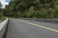 this is a long paved highway next to some trees and hills with tall, gray boulders and trees