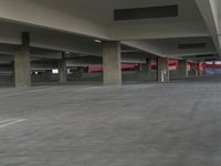 large empty parking garage with concrete pillars on either side and red light inside of it