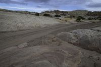 the view of a dirt road from the top of a hill covered with rocks and scrub