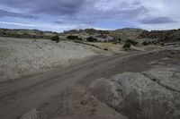 the view of a dirt road from the top of a hill covered with rocks and scrub