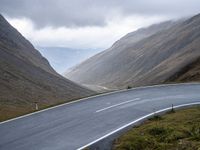 the curved asphalt road is flanked by large mountains and cloudy skies with clouds in the sky