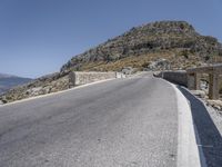 a man rides his bike on a road through the mountains by rocks and stone fences