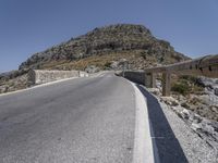 a man rides his bike on a road through the mountains by rocks and stone fences