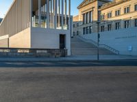 empty street lined with cement buildings next to a tall building with a staircase up to it