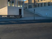 empty street lined with cement buildings next to a tall building with a staircase up to it