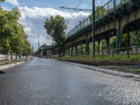 a train traveling down a train track next to a bridge on a street side in front of trees and sky