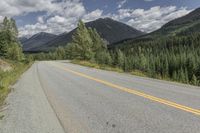 a long straight road with a yellow line next to a tree covered mountain valley and blue skies