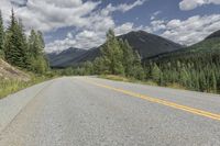 a long straight road with a yellow line next to a tree covered mountain valley and blue skies